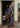 At Home With Ray Cactus Rose Silky Ribbon Scarf in Saguaro sage green worn as a neck scarf by a woman in a denim shirt and jeans, standing in a doorway with a saddle, styled in a relaxed long tie.