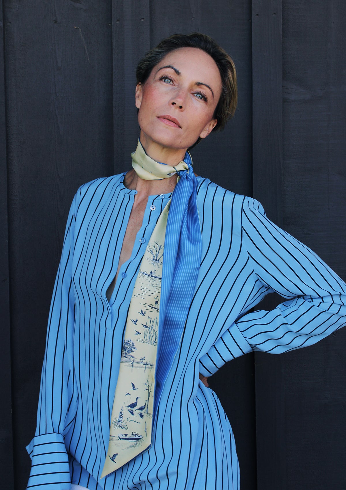 Woman wearing a long silk ribbon scarf with a bright blue pinstripe on one side and a delightful lake scene rendered in a traditional toile pattern