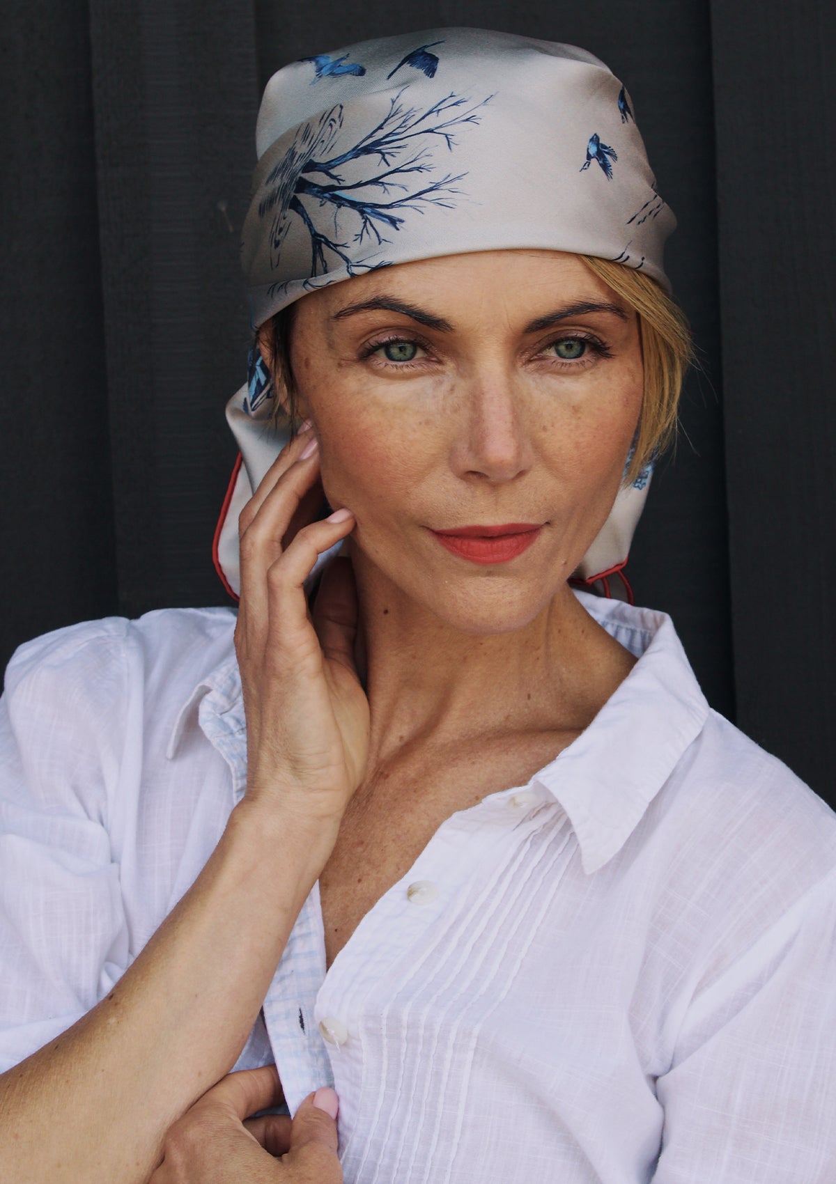 Woman wearing a silk head scarf in pale grey with dark blue illustrations and bright red trim