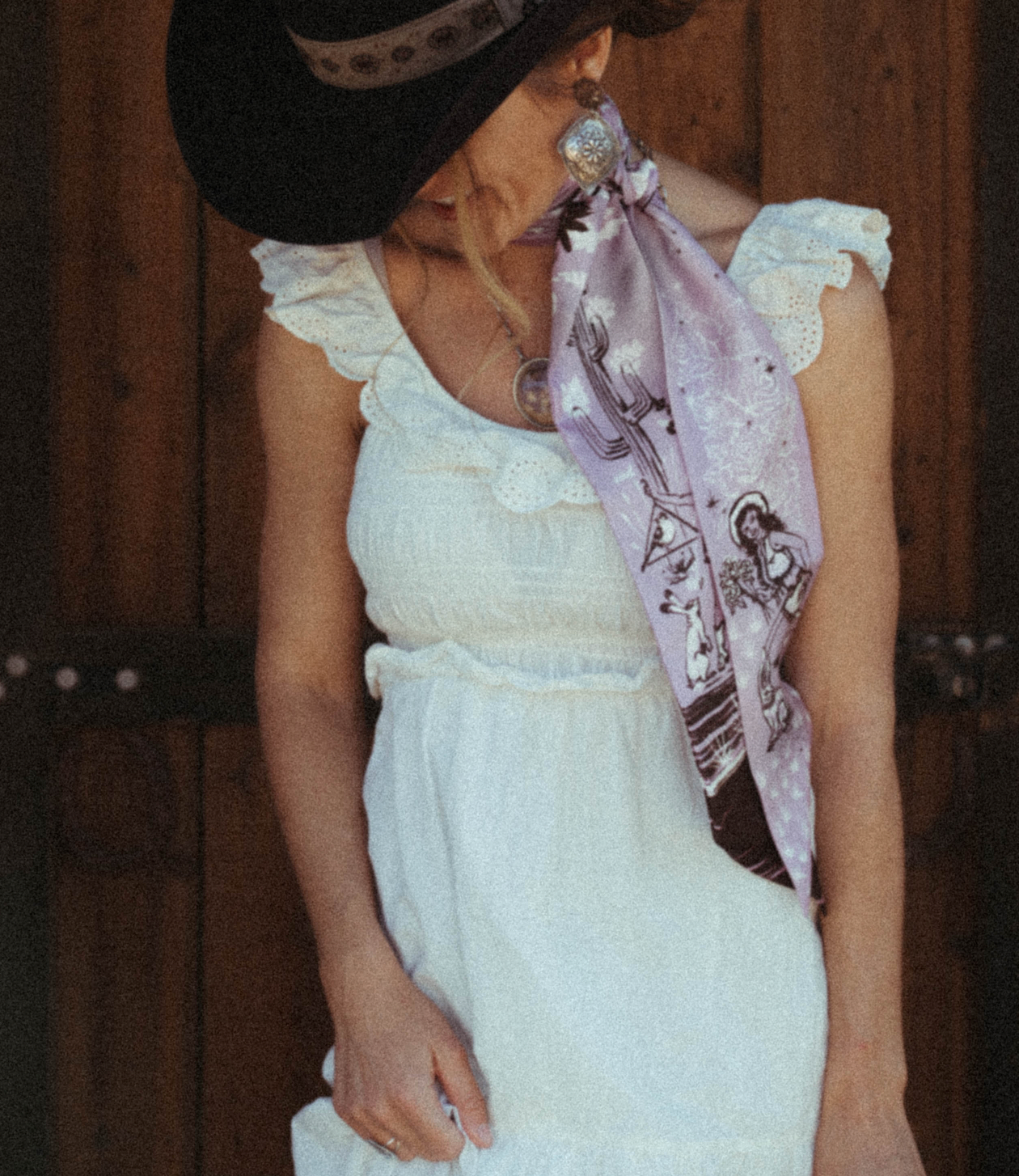 Woman in a summery white dress wearing a lilac and henna brown cowgirl illustrated ribbon scarf 