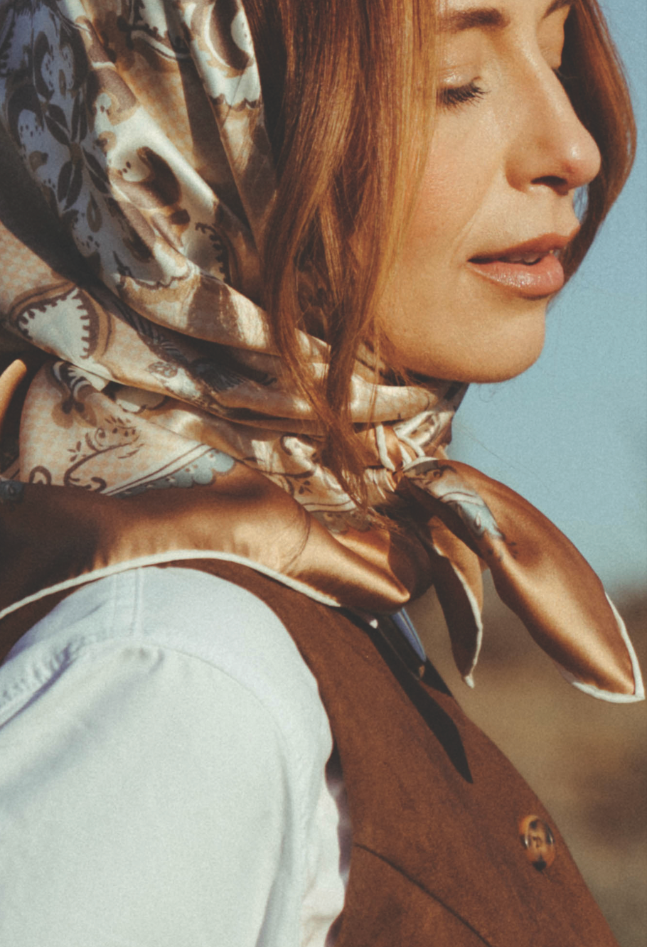 Woman wearing a neutral and soft blue patterned scarf with a blurred natural background