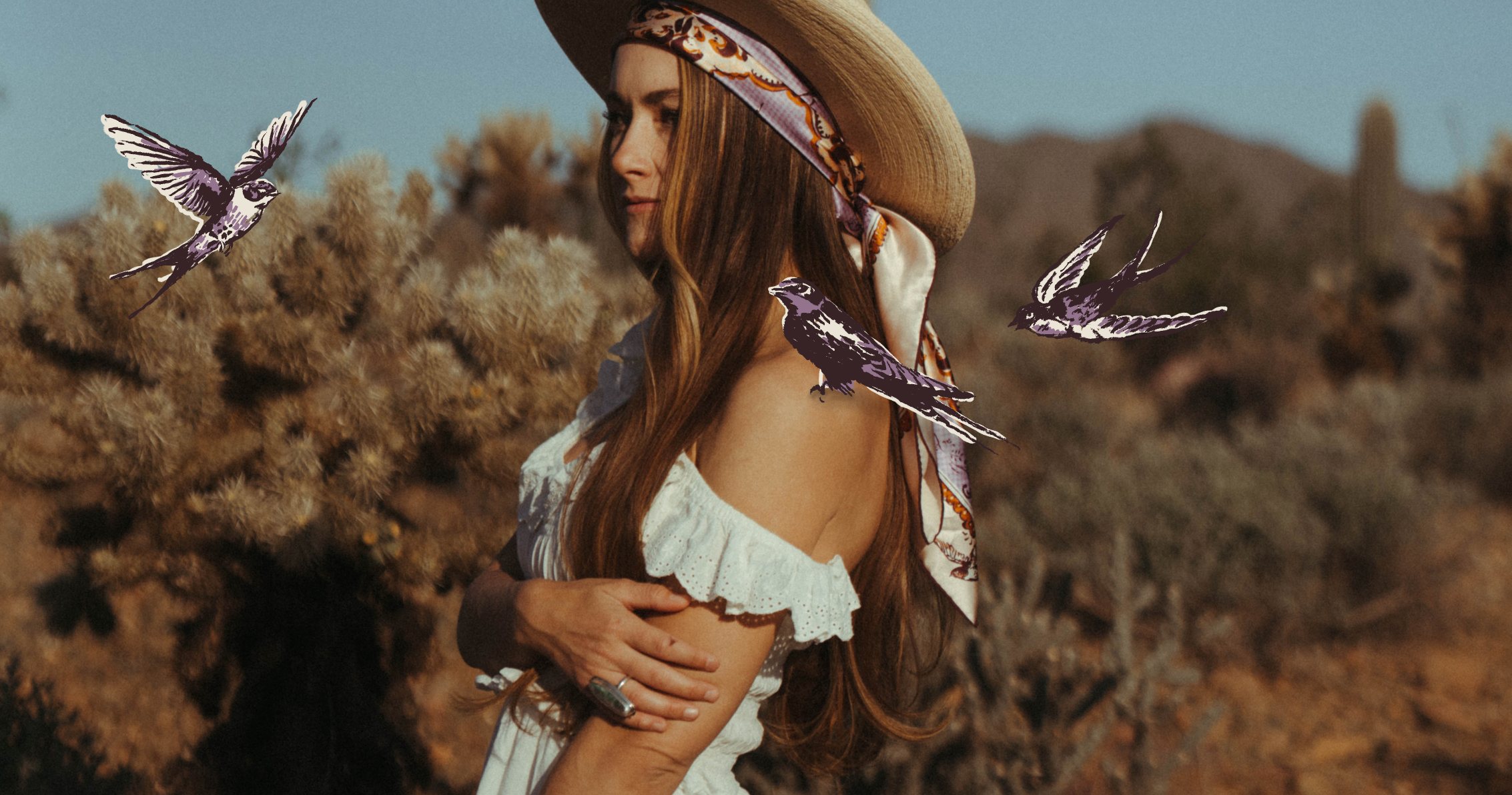 Woman in a desert setting with birds and a hat wearing a lilac and russet print silk scarf draping down her back