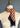 Corn Dancer in Flame" by At Home With Ray is elegantly draped around the neck. The brown and beige houndstooth-patterned scarf, with frayed edges, mirrors the intricate designs of a Corn Dancer costume. The fabric's pattern is clearly visible.